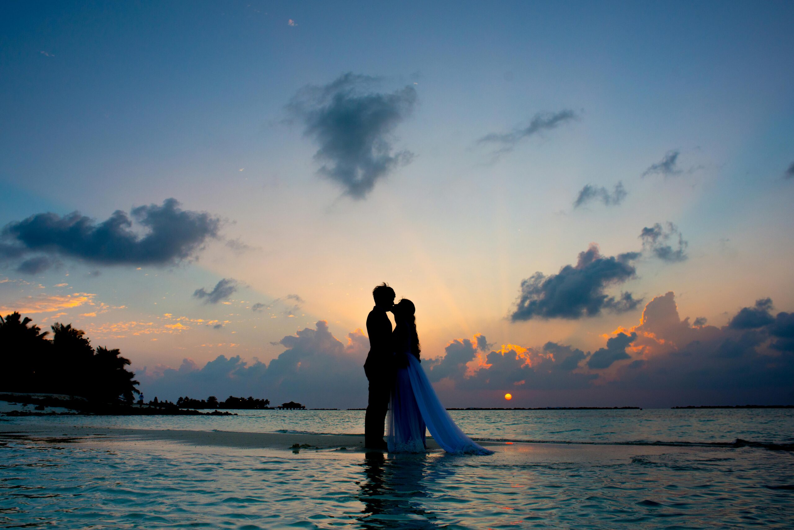 A couple shares a romantic moment on a tropical beach during a beautiful sunset, symbolizing love and serenity.