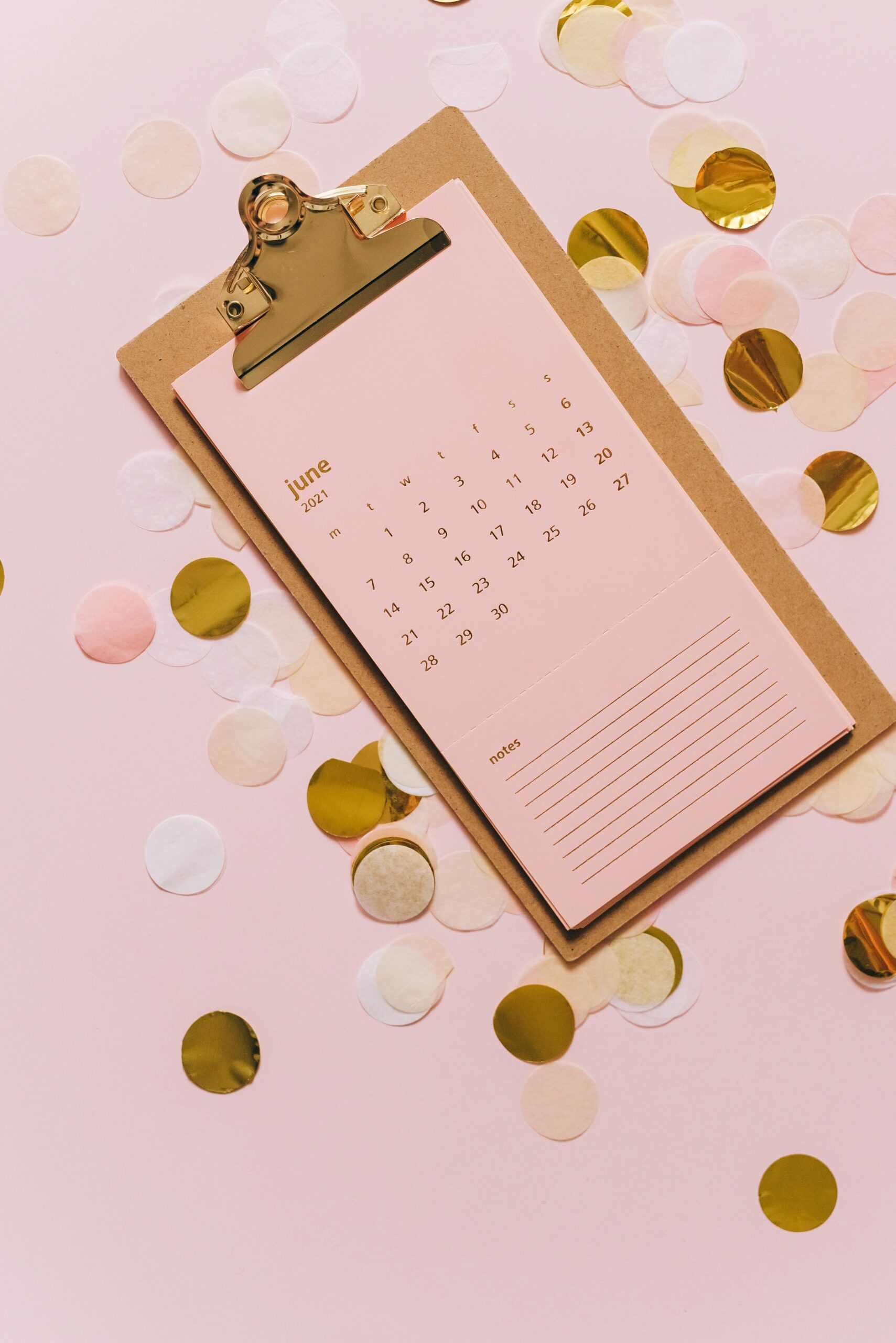 Aesthetic pink clipboard with a June calendar surrounded by festive confetti on a pastel background.