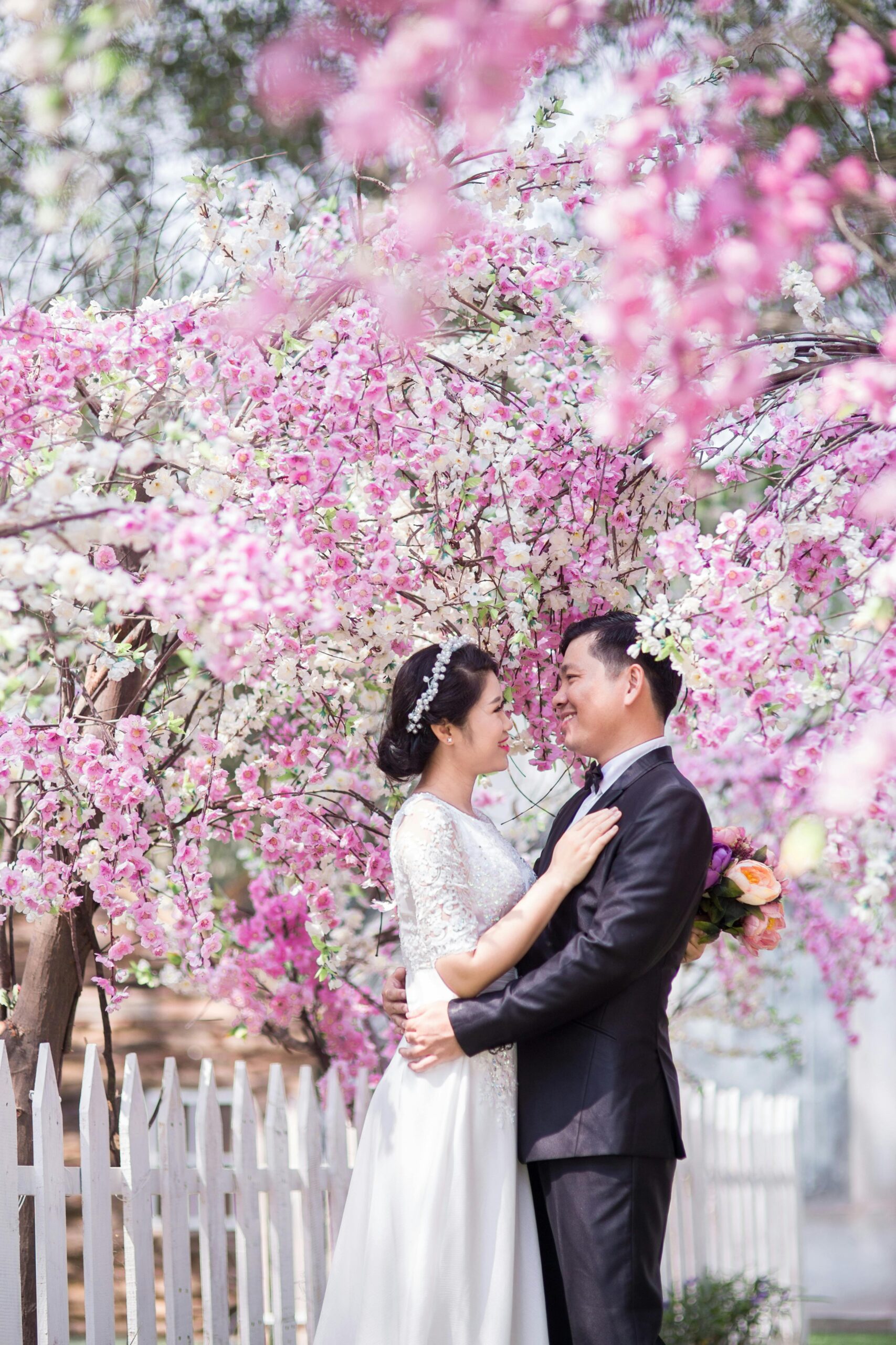 Elegant couple poses under cherry blossoms for a memorable wedding photoshoot.
